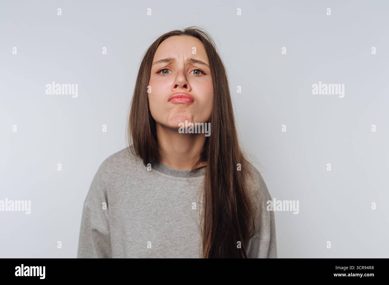 Junge Frau zeigt Unmut durch Stirnrunzeln, zeigt eine komplexe Mischung von Emotionen auf weißem Hintergrund Stockfoto