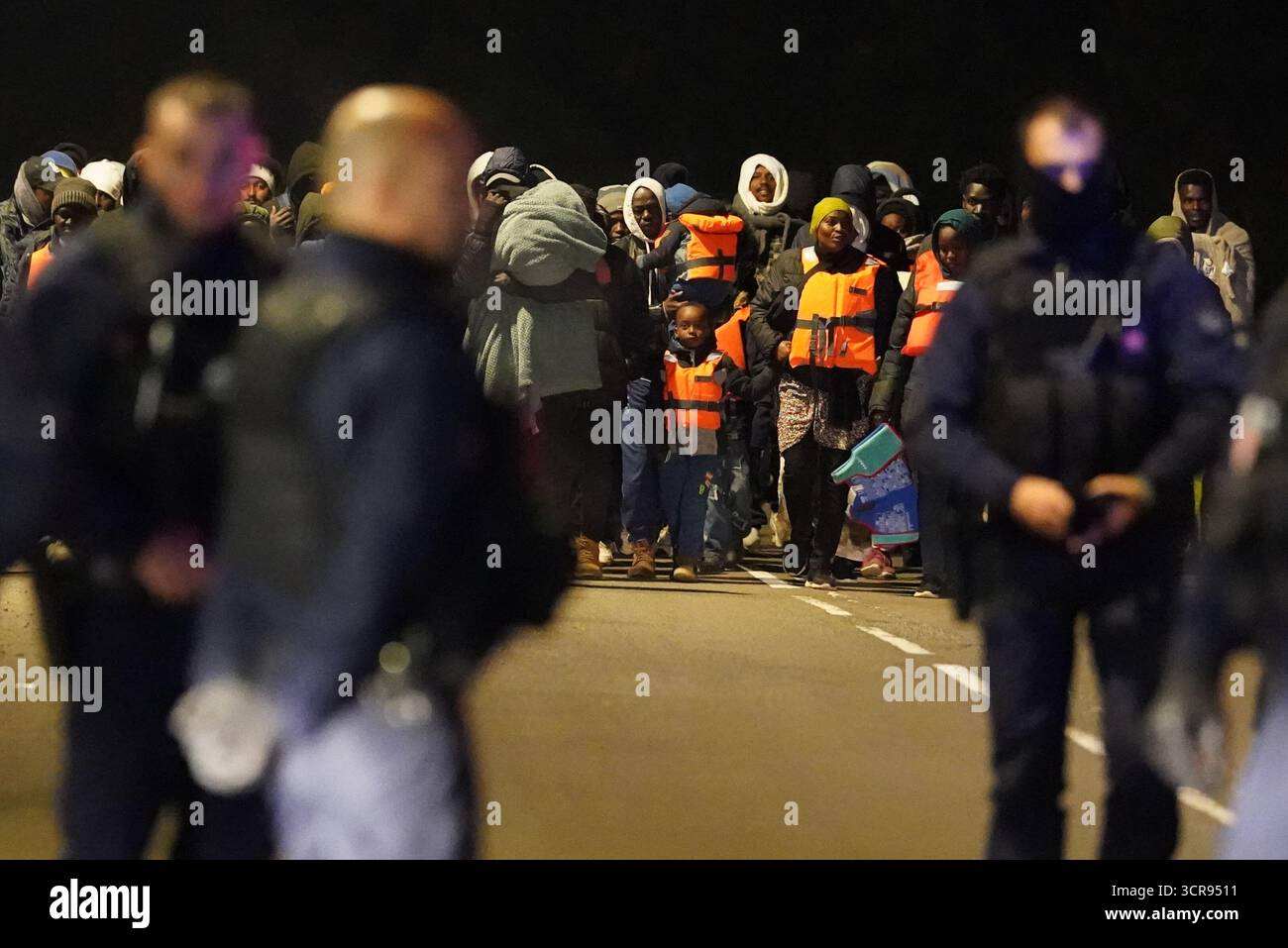 HINWEIS DER REDAKTION: Der PA Picture Desk konnte nicht die erforderliche Erlaubnis erhalten, Kinder unter 16 Jahren zu fotografieren, die sich auf ihr Wohlergehen beziehen. Dieses Bild wurde nicht pixeliert bereitgestellt, damit Kunden in ihrem eigenen Stil pixelieren können. Französische Polizeibeamte beobachten eine Gruppe von Menschen in der Nähe eines Kanals in Gravelines, Frankreich, wo Migranten versuchen, an Bord eines kleinen Bootes zu gehen, um den Ärmelkanal zu überqueren. Bilddatum: Dienstag, 30. September 2025. Stockfoto