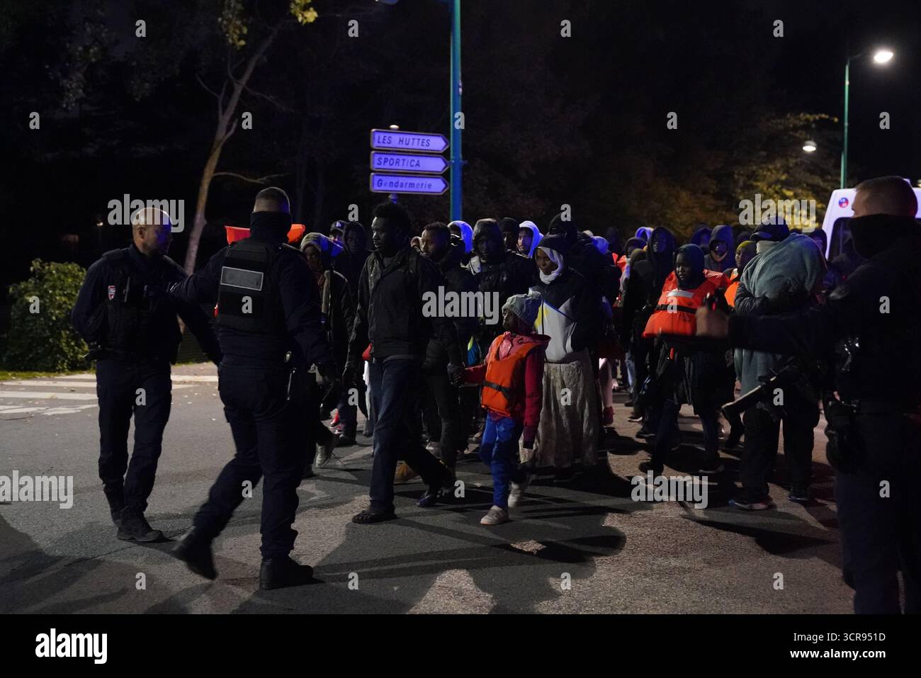HINWEIS DER REDAKTION: Der PA Picture Desk konnte nicht die erforderliche Erlaubnis erhalten, Kinder unter 16 Jahren zu fotografieren, die sich auf ihr Wohlergehen beziehen. Dieses Bild wurde nicht pixeliert bereitgestellt, damit Kunden in ihrem eigenen Stil pixelieren können. Französische Polizeibeamte eskortieren eine Gruppe von Menschen in der Nähe eines Kanals in Gravelines, Frankreich, wo Migranten versuchen, an Bord eines kleinen Bootes zu gehen, um den Ärmelkanal zu überqueren. Bilddatum: Dienstag, 30. September 2025. Stockfoto