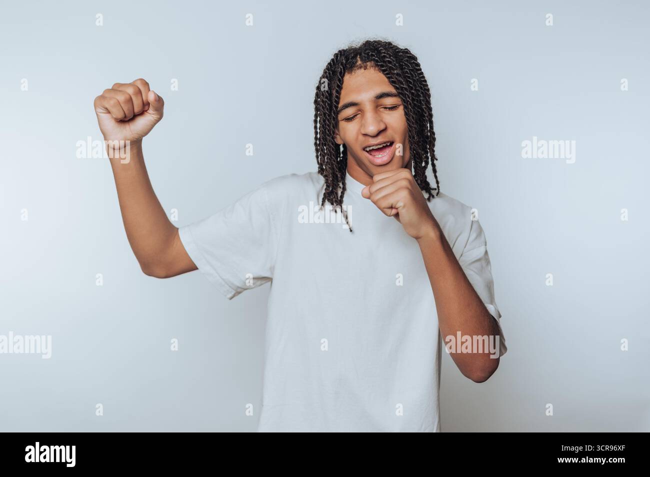 Der junge Mann singt fröhlich mit einer verspielten Pose und verkörpert Glück und unbeschwerten Geist auf weißem Hintergrund Stockfoto