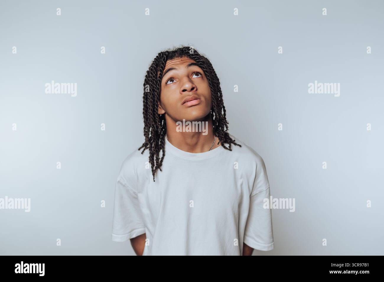 Der junge Mann blickt mit einem kontemplativen Ausdruck nach oben und ruft Neugier und Introspektion auf weißem Hintergrund hervor Stockfoto