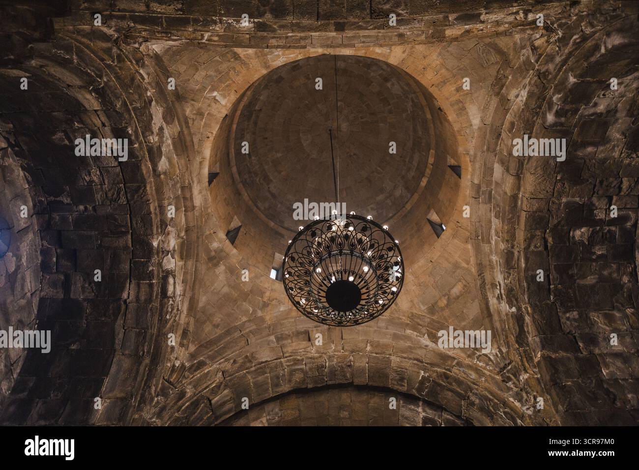Blick auf den kunstvoll verzierten Kronleuchter, der von einer Steinkuppel im Tatev-Kloster hängt und Schatten auf die alten Wände wirft, Tatev-Kloster, Provinz Syunik, Armenien. Stockfoto