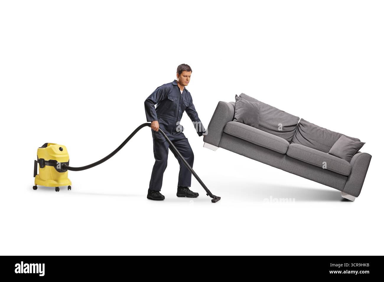 Männlicher Wartungsreiniger mit einem Staubsauger unter einem Sofa isoliert auf weißem Hintergrund Stockfoto