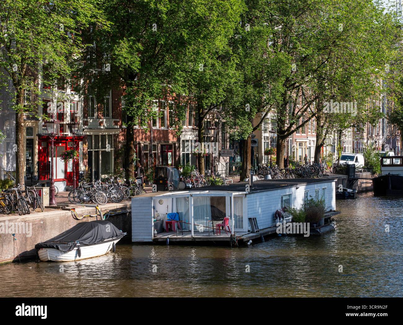Farbenfrohe Hausboote liegen friedlich entlang eines Kanals, umgeben von Bäumen. Stockfoto