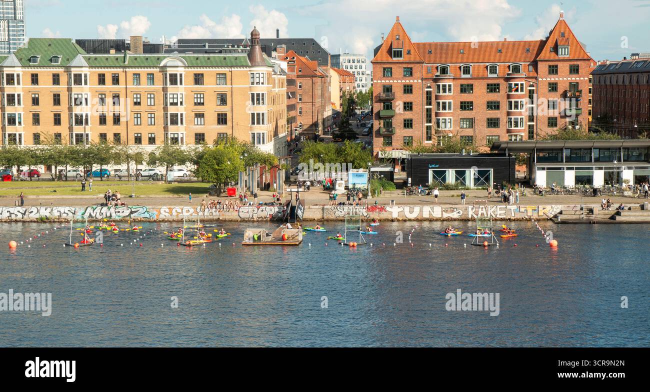 Nyhavn, Kopenhagen, Dänemark - 2. August 2025: Farbenfrohe Kajakboote gleiten unter klarem blauen Himmel entlang der Uferpromenade. Stockfoto
