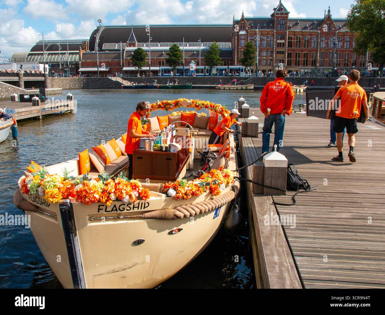 Amsterdam, Niederlande - 5. August 2025: Touristen steigen an einem belebten Ort am Wasser an Bord eines festlich geschmückten Bootes. Stockfoto