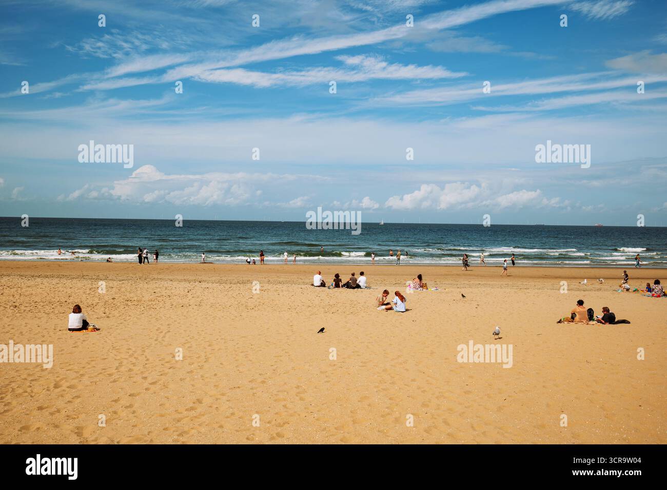 Die Menschen am Strand genießen die letzten Sommertage. Sonniger blauer Himmel mit dünnen Wolken, Weitwinkelblick Stockfoto