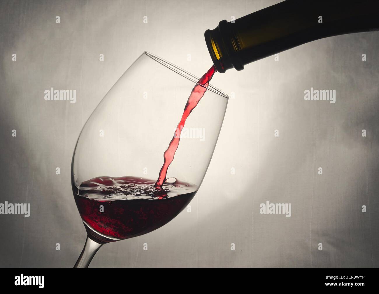 Rotwein wird in ein Stängelglas gegossen. Eine Flasche Rotwein gießt einen Strom Wein in ein Weinglas, vor hellem Hintergrund. Weinblase Stockfoto