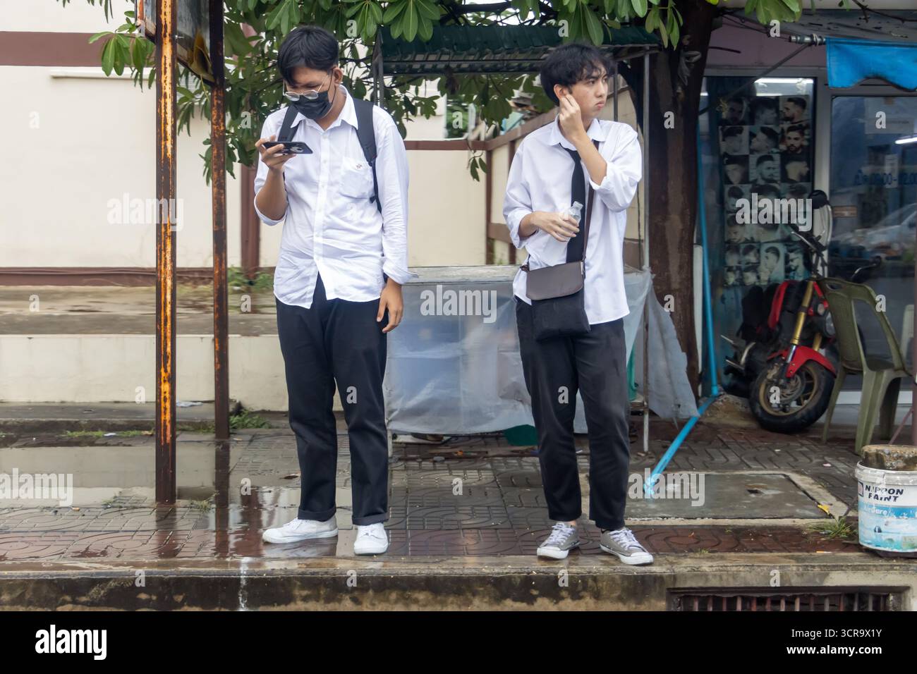 BANGKOK, THAILAND, 06. Oktober 2024, zwei junge Männer warten bei regnerischem Wetter an einer Bushaltestelle in einem Stadtgebiet Stockfoto