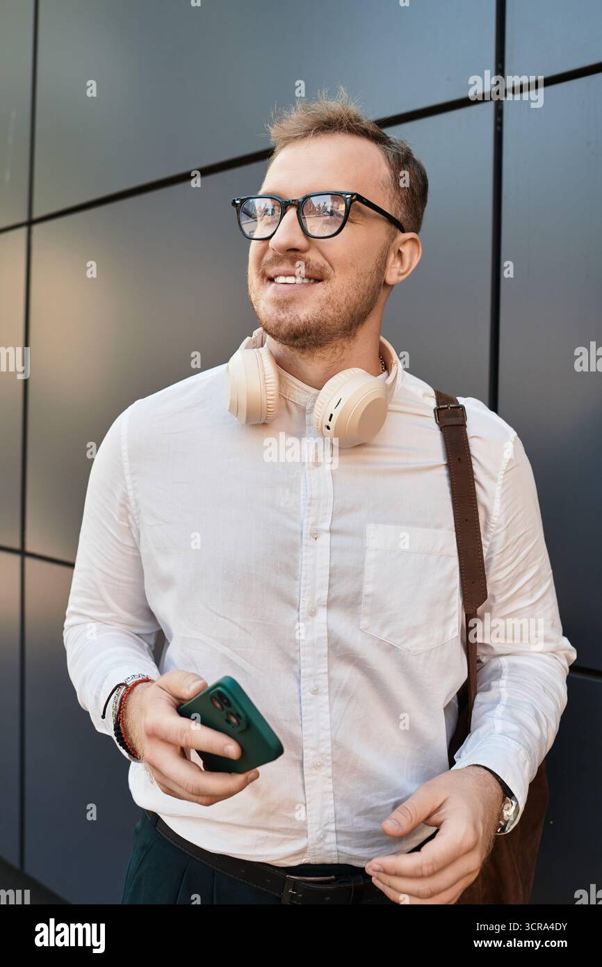 Ein junger männlicher Lehrer steht draußen, trägt Brille und Kopfhörer und genießt einen Moment der Freude. Stockfoto