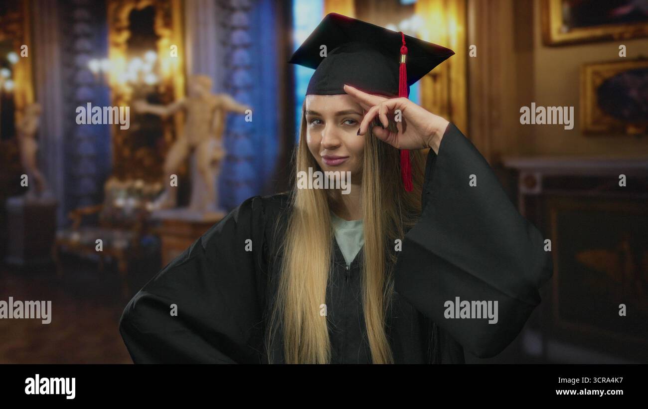 Die junge Frau im Abschlusskleid posiert selbstbewusst in einem eleganten Museum, das Kunst- und Kulturhighlights zeigt. Stockfoto