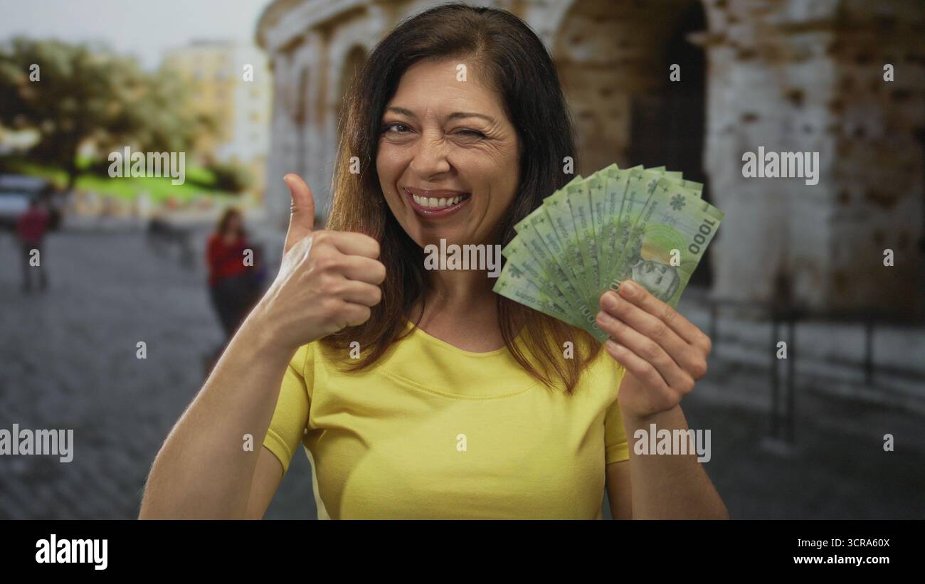 Die Frau im Mittelalter zeigt chilenische Peso-Banknoten mit Daumen nach oben beim Bau am kolosseum; Vertrauen in die Tourismusfinanzierung. Stockfoto