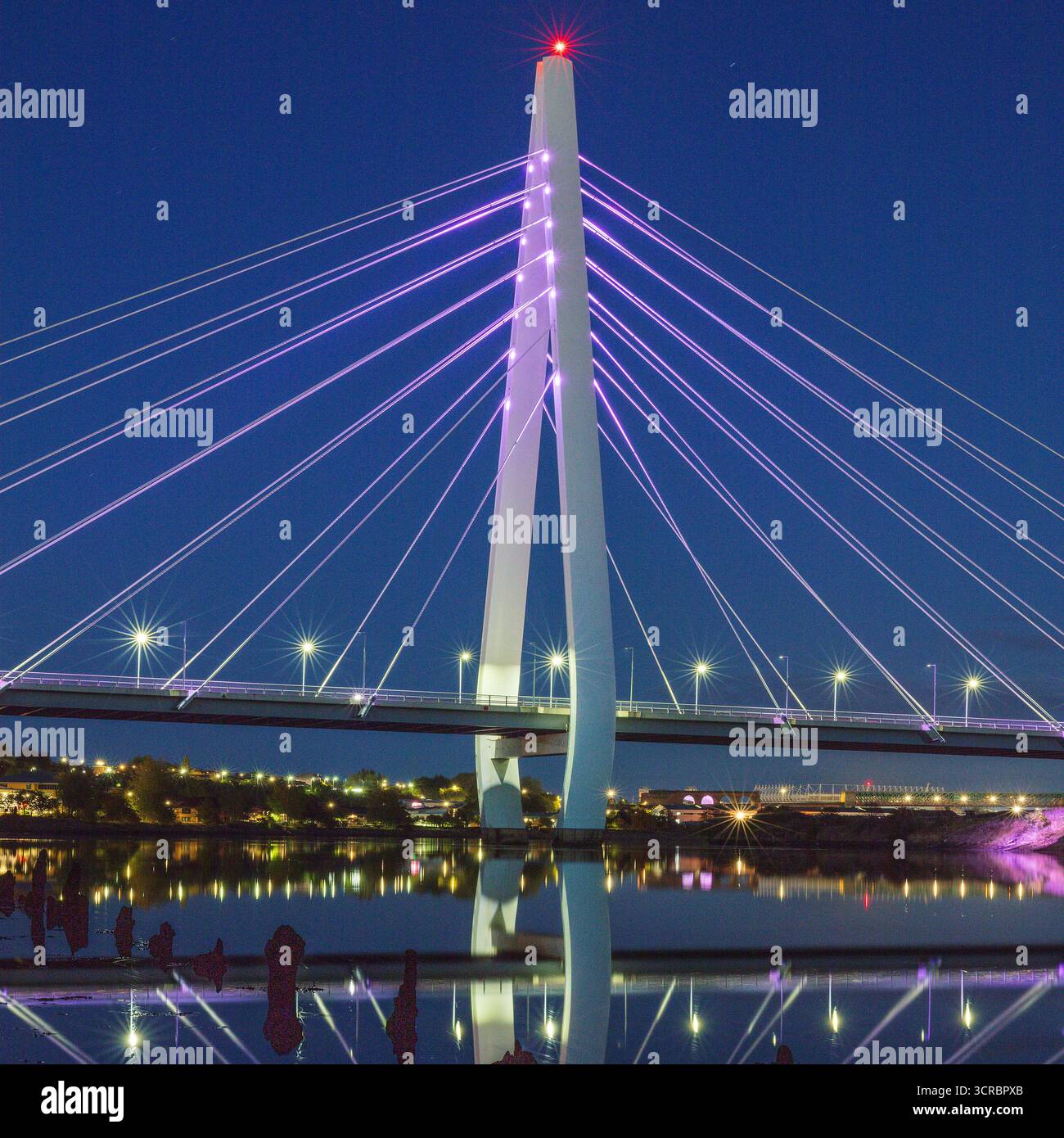 Ein Blick in die Dämmerung der beleuchteten Northern Spire Bridge in Sunderland, die sich im River Wear spiegelt und flussabwärts in Richtung Stadtzentrum blickt Stockfoto