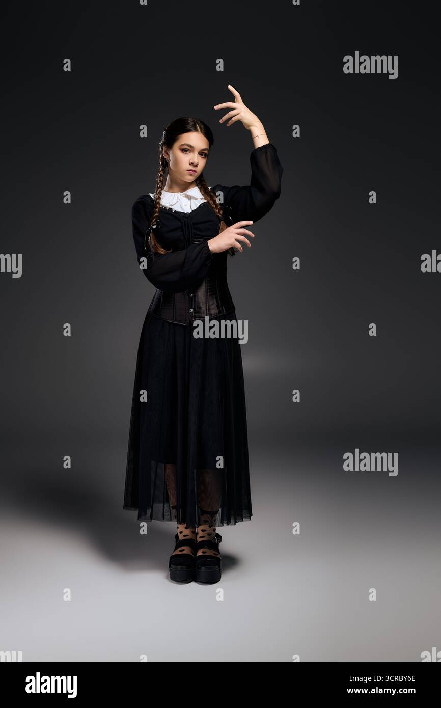 Ein Mädchen mit Zöpfen posiert in einem Gothic-Kleid, das von einer gruseligen Mittwochfigur zu Halloween inspiriert ist. Stockfoto
