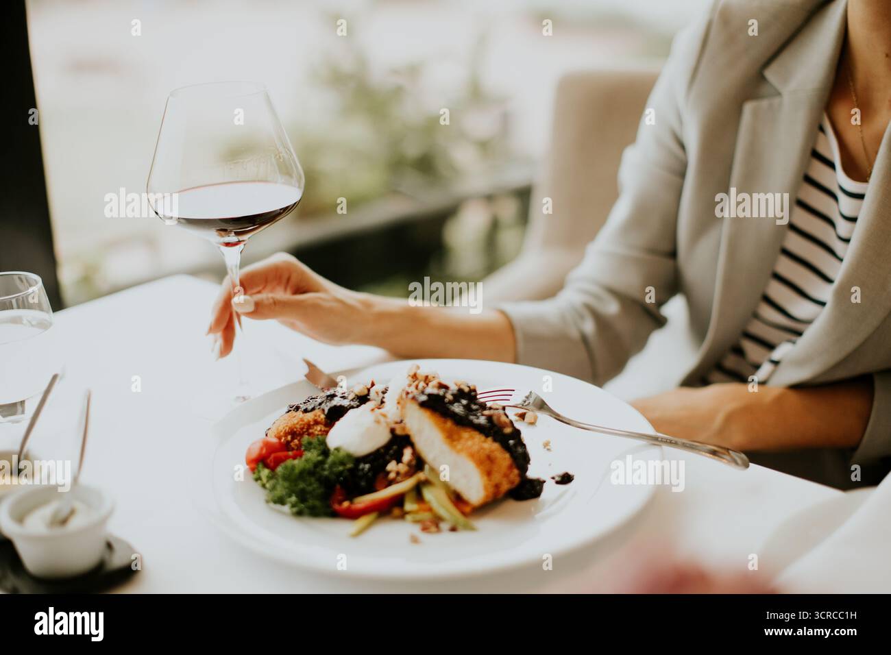 Gäste entspannen sich in einem schicken Restaurant und genießen ein herrlich gekochtes Hühnchengericht mit einer reichhaltigen Sauce und einem Glas Rotwein während eines eleganten Abendabends Stockfoto