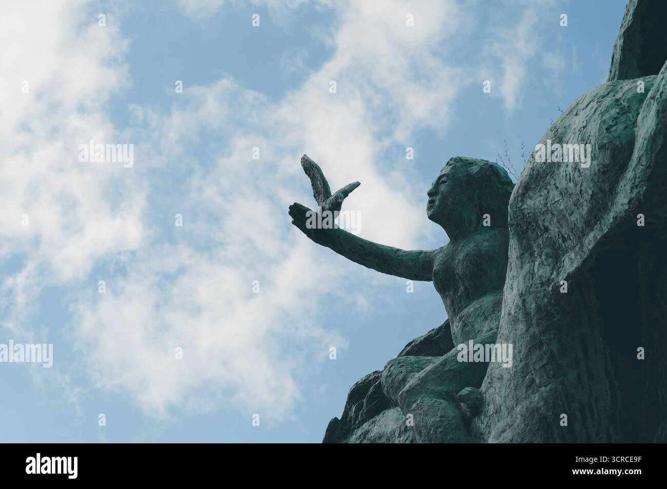 Bronzestatue einer Frau, die einen Vogel freilässt, vor einem blauen Himmel mit verstreuten Wolken Stockfoto