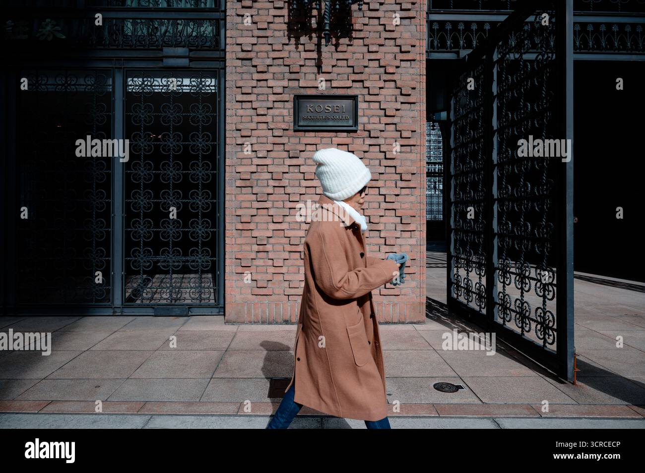 Eine Person mit weißem Hut und braunem Mantel geht an der Backsteinfassade des Kosei-Gebäudes in Osaka vorbei Stockfoto