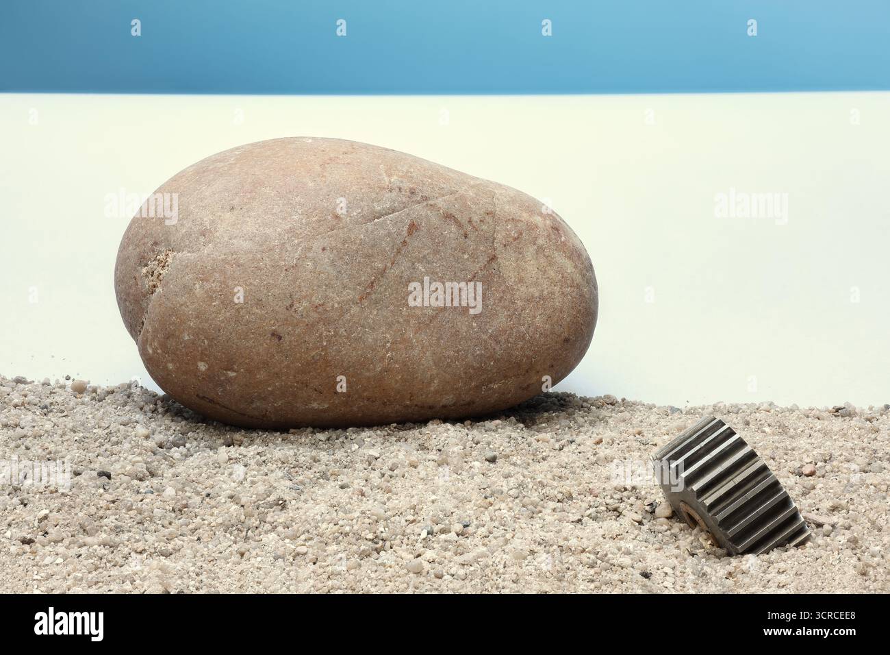 Einfaches Stillleben mit drei Gegenständen – zwei natürliche und ein künstlich geschaffene: Zahnrad, Stein und Sand. Foto mit maximaler Schärfentiefe. Stockfoto