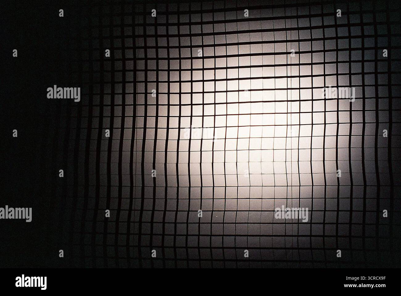 Großes schwarzes Rastermuster, das das gesamte Bild überzieht, durch ein Streufilter von einem Scheinwerfer beleuchtet, auf Analogfilm aufgenommen. Stockfoto