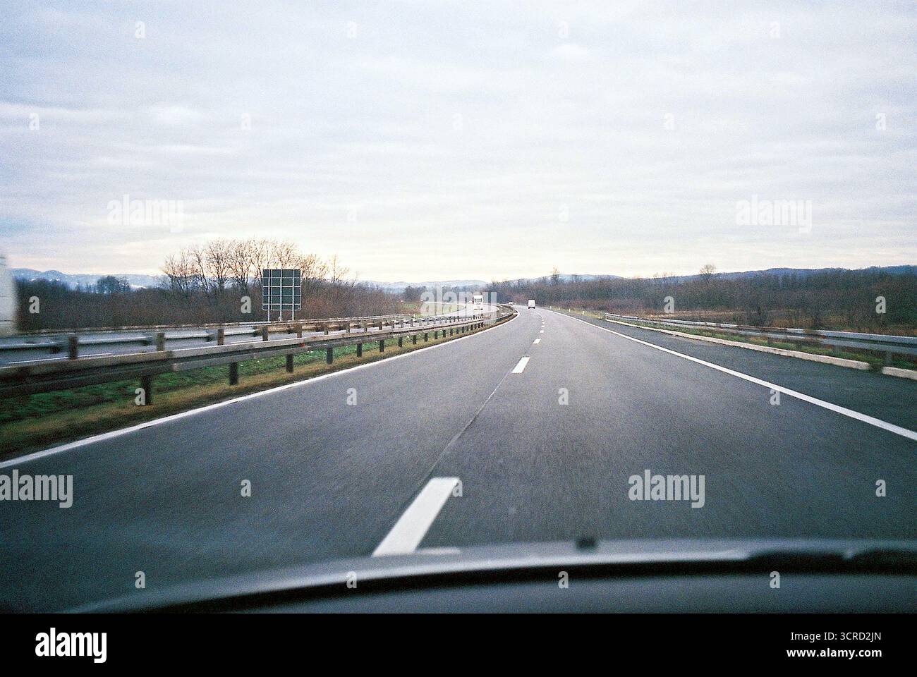 Analoges 35-mm-Foto aus Sicht des Fahrers auf einer leeren Autobahn unter bewölktem Himmel. Sanfte Töne, offene Straße, ruhig und atmosphärisch. Stockfoto