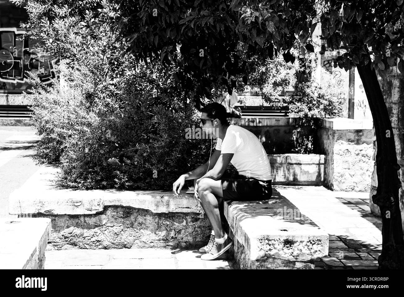 Mann, der allein auf einer Steinbank unter Baumschatten in Athen sitzt, in Schwarz-weiß-Straßenfotografie. Stockfoto