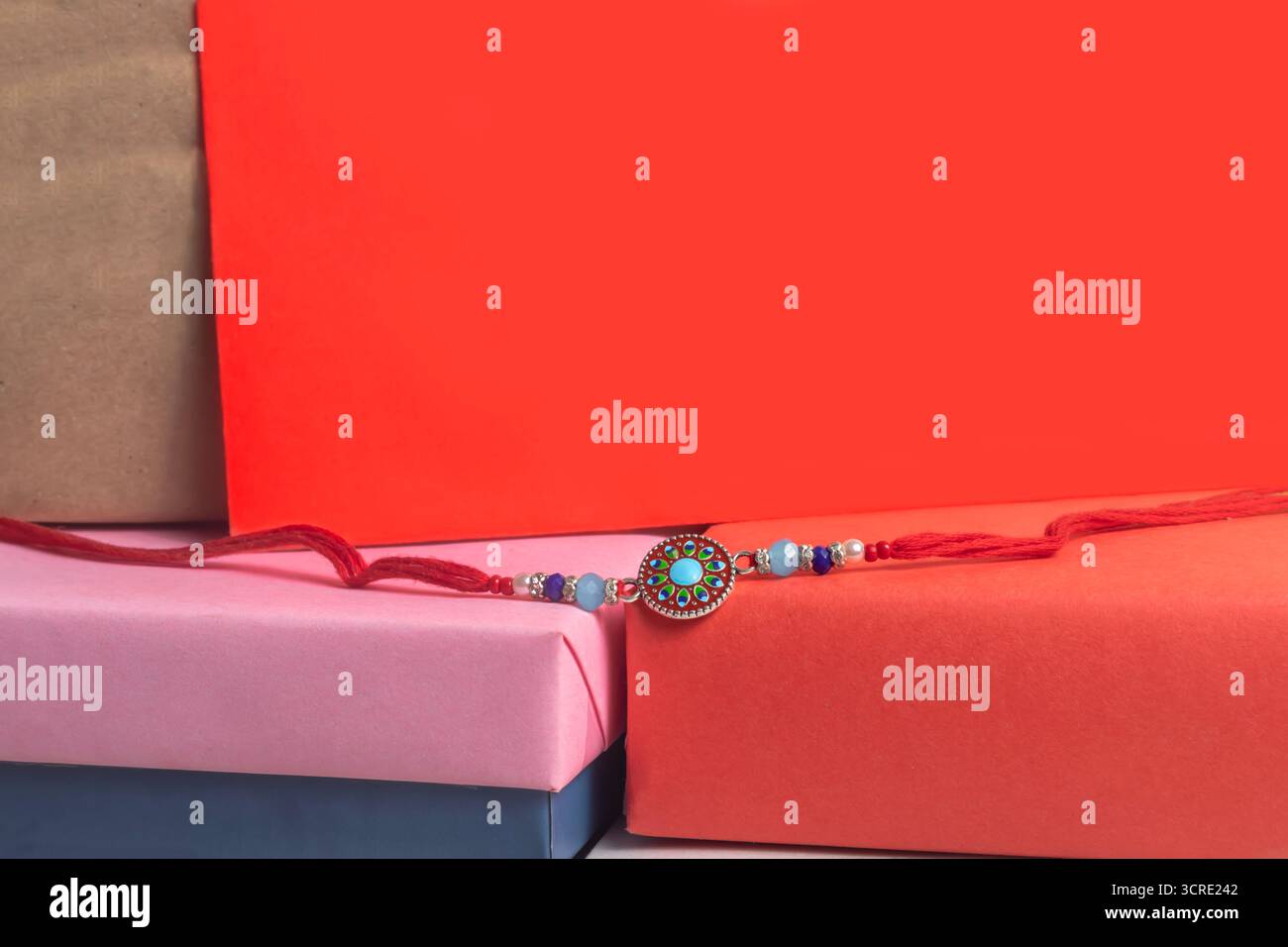 Ein zartes rotes Armband mit türkisfarbenen und blauen Perlen und ein dekorativer Kreisanhänger für Raksha Bandhan-Feierlichkeiten befindet sich in einer lebendigen Geschenkbox Stockfoto