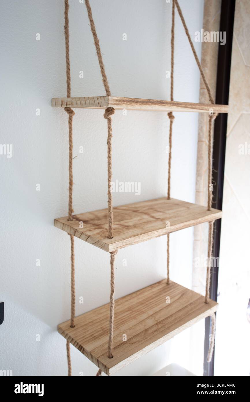 Blick auf ein dekoratives Holzregal, das durch ein Seil zusammengehalten wird und an der Wand montiert ist. Stockfoto