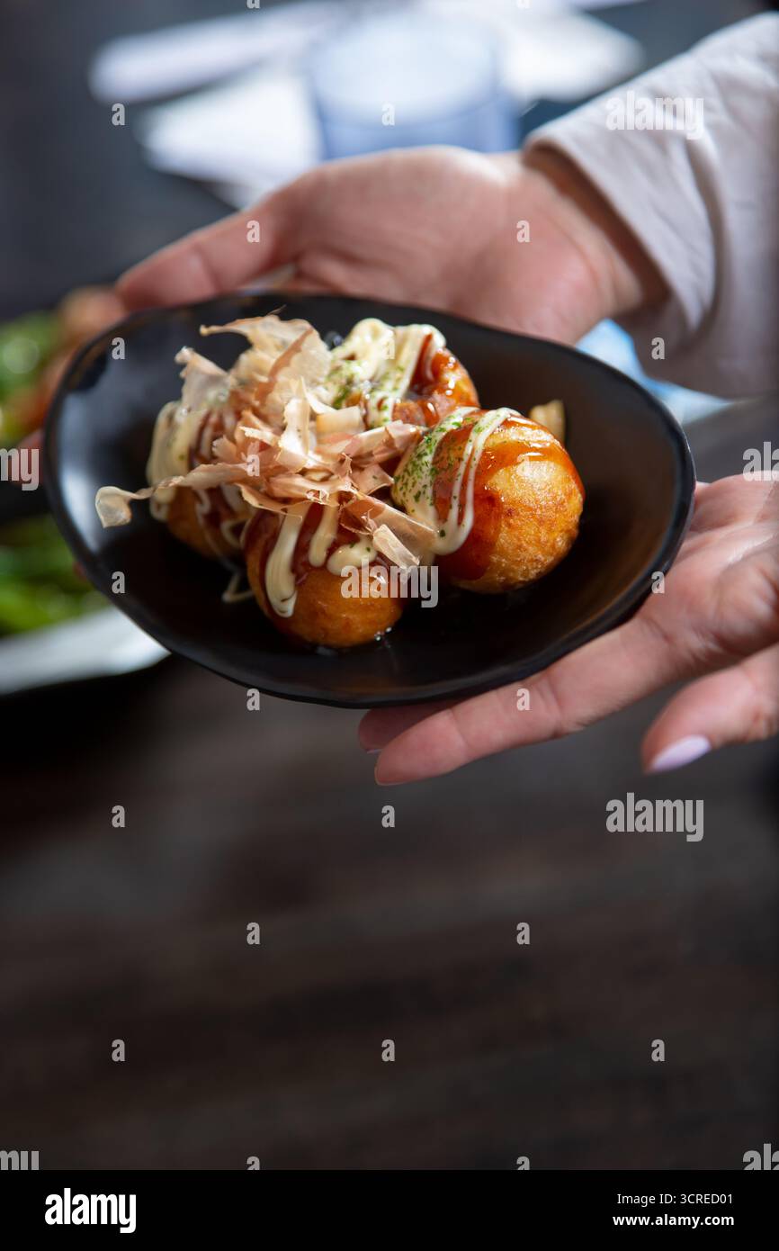 Ein Blick auf die Hände, die einen Teller Takoyaki halten. Stockfoto