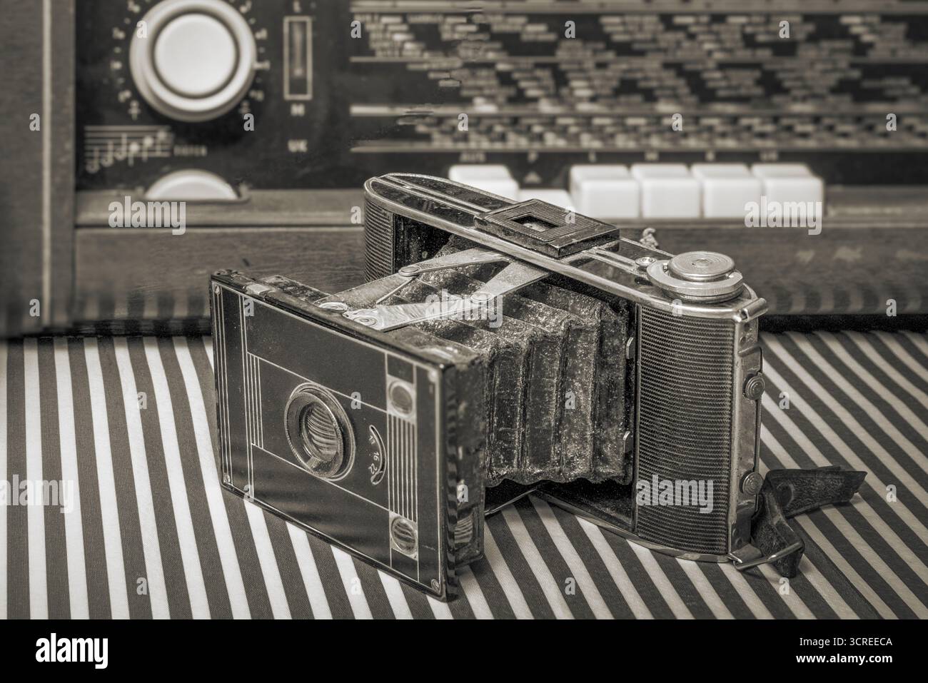 Vintage-Kamera. Einziehbare Akkordeonlinse. Vor dem Hintergrund eines alten Röhrenradios. Schwarz-weiß Stockfoto