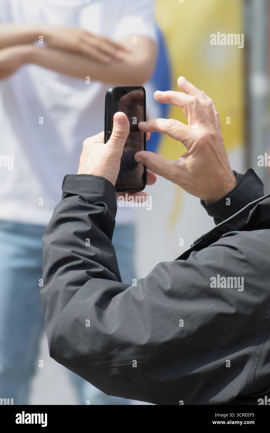 Hände eines älteren Mannes, der eine Veranstaltung auf einem Smartphone filmt Stockfoto