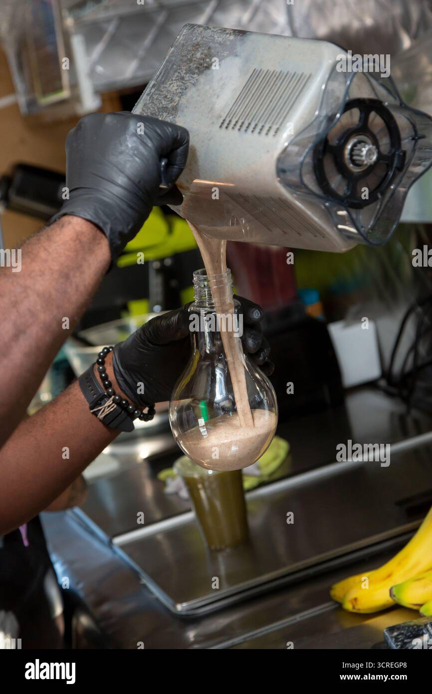 Ein Blick auf die Hände, die Smoothie-Inhalt aus einem Mixkrug in eine Glühbirne gießen. Stockfoto