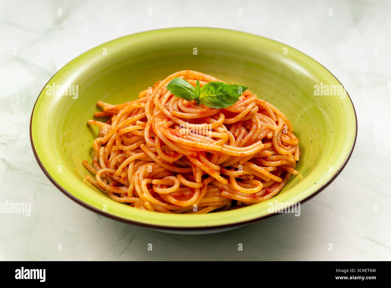 Italienische Spaghetti-Pasta in einer grünen Schüssel, belegt mit frischem Basilikumblatt Stockfoto
