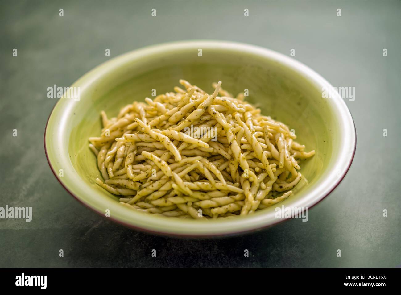 Trofie-Pasta mit Pesto-Sauce in einer grünen Schüssel, die italienische kulinarische Tradition repräsentiert Stockfoto