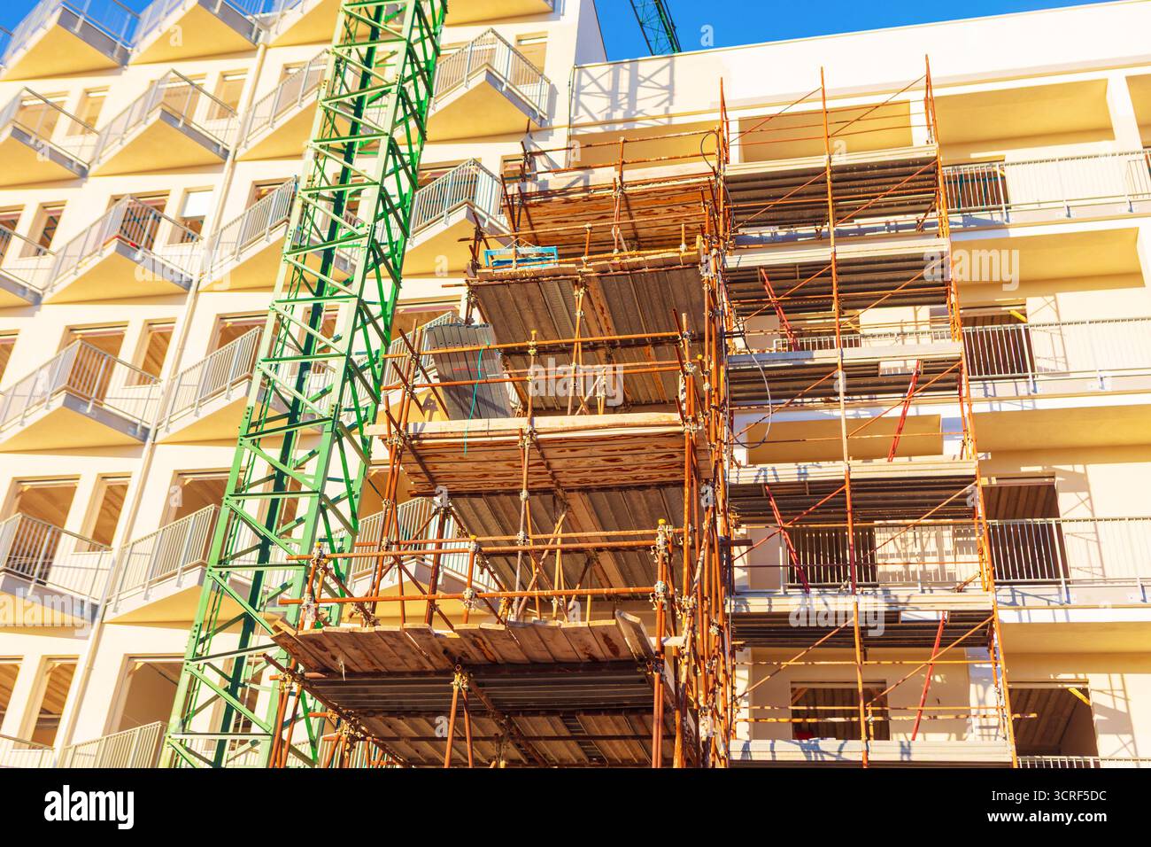 Aktive Baustelle mit großem Wohngebäude, umfangreichem Metallgerüst und Baukran. Temporäre Strukturen Stockfoto