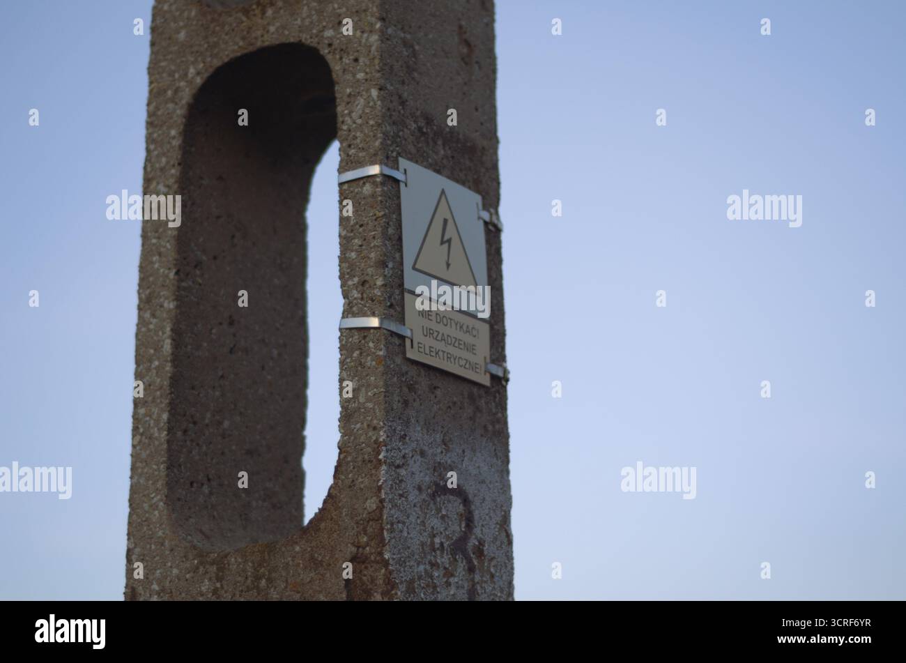 Betonmasten mit „nicht berühren“-Schild in Polnisch, einheitlicher Himmel Hintergrund, Sonnenuntergang Stockfoto