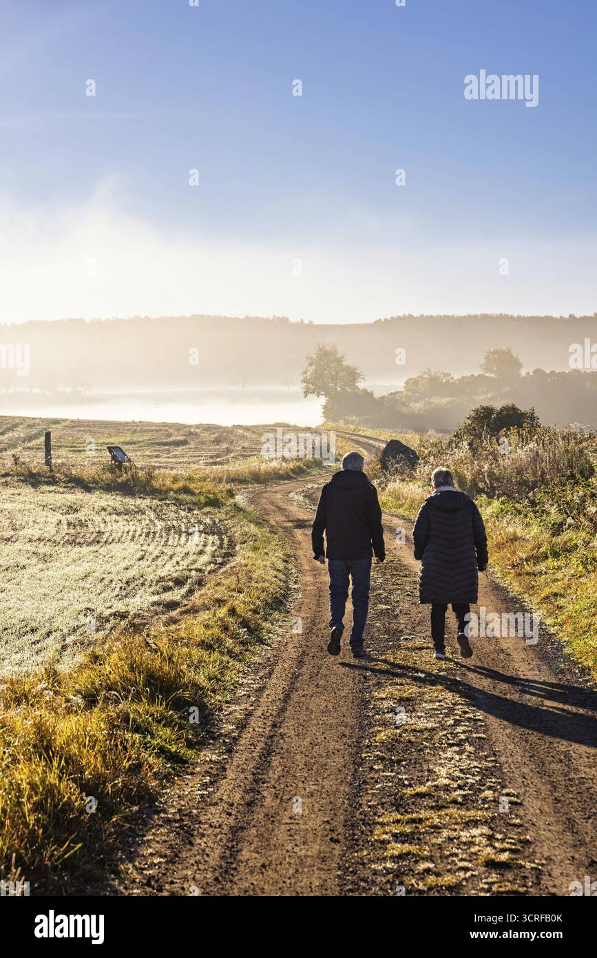 Zwei Leute laufen auf Schotterwegen auf dem Land an einem nebeligen Herbstmorgen, Schweden Stockfoto