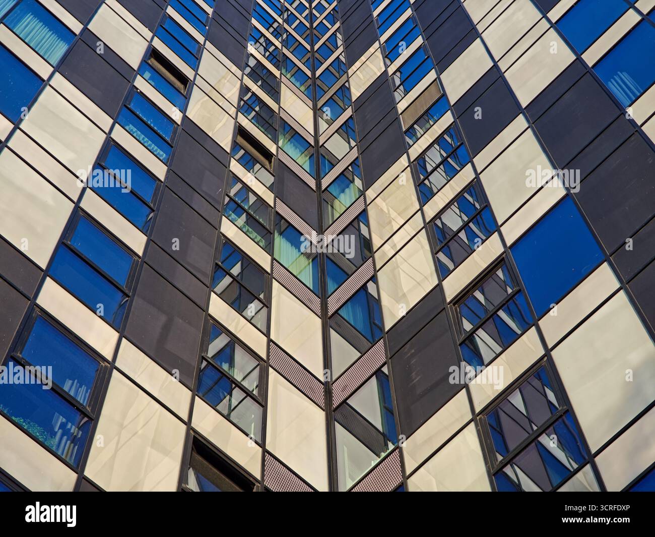 Abstrakte Ansicht einer modernen Wolkenkratzerfassade mit einem sich wiederholenden Schachbrettmuster aus dunklen Paneelen und reflektierenden Fenstern in Blau- und Weißtönen Stockfoto