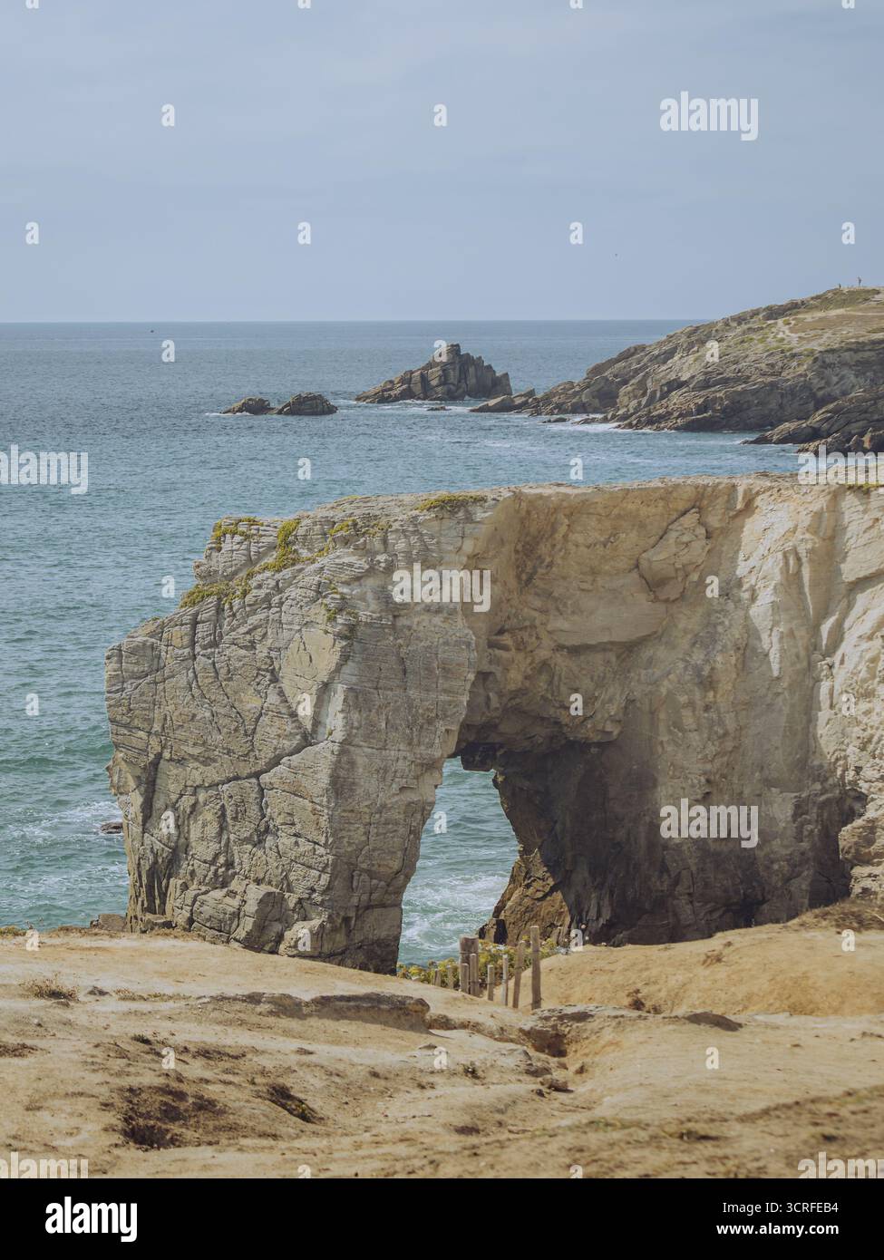 Blick auf einen natürlichen Bogen Arche de Port Blanc Roche Percée, der von der unerbittlichen Umarmung des Ozeans geschnitzt wurde und als Wächter gegen das türkisfarbene Wasser steht, Saint-Pierre-Quiberon, Bretagne, Frankreich. Stockfoto