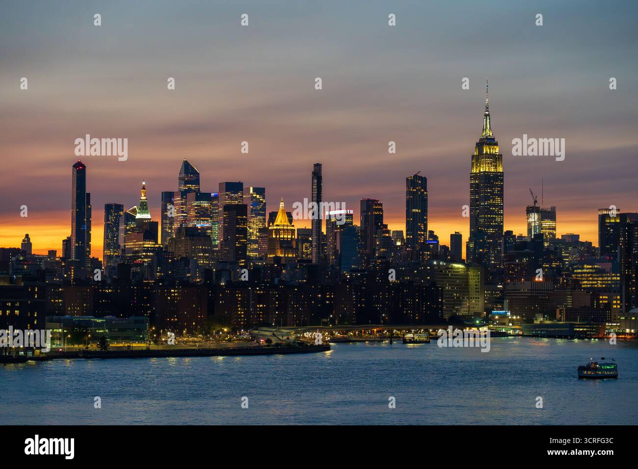 Juli. Blick auf die beleuchtete Skyline, die in der Abenddämmerung durchdringt, während der Fluss das Leuchten der Stadt am 4. Juli reflektiert, New York, USA. Stockfoto