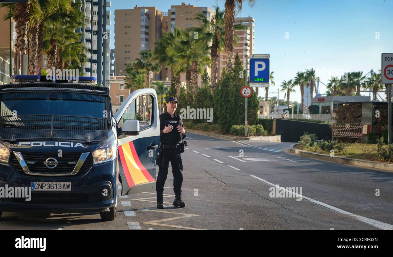Sonniger Tag mit einem Polizisten in Uniform, der neben einem Polizeiwagen auf der Straße steht, möglicherweise den Verkehr managt oder einen Kontrollpunkt durchführt. Der Van ha Stockfoto