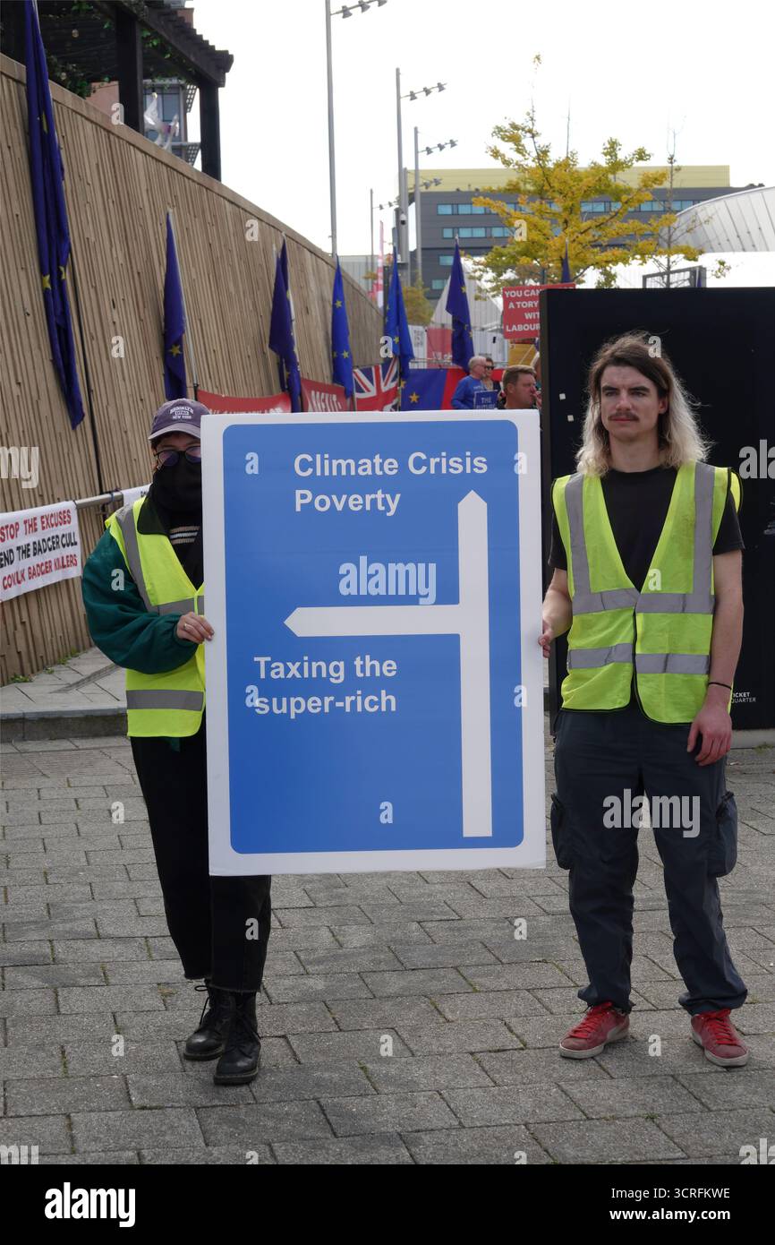 Zwei Demonstranten in hoch sichtbaren Westen halten während einer politischen Demonstration ein großes blaues Schild mit der Aufschrift "Klimakrise, Armut, Besteuerung der Superreichen". Stockfoto