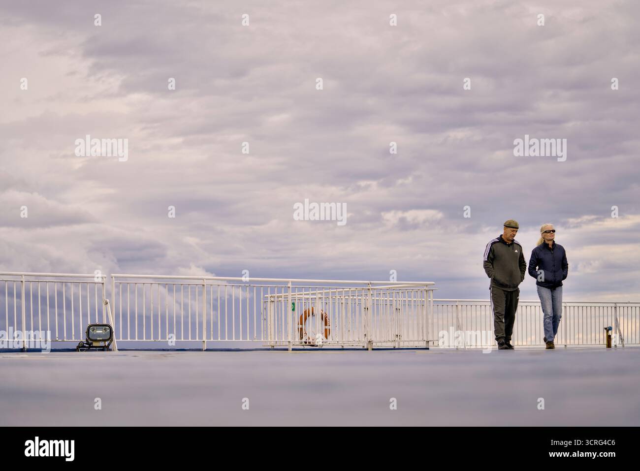 Zwei Personen spazieren gemütlich auf einer Terrasse unter einem riesigen und dramatischen Himmel voller Wolken Stockfoto