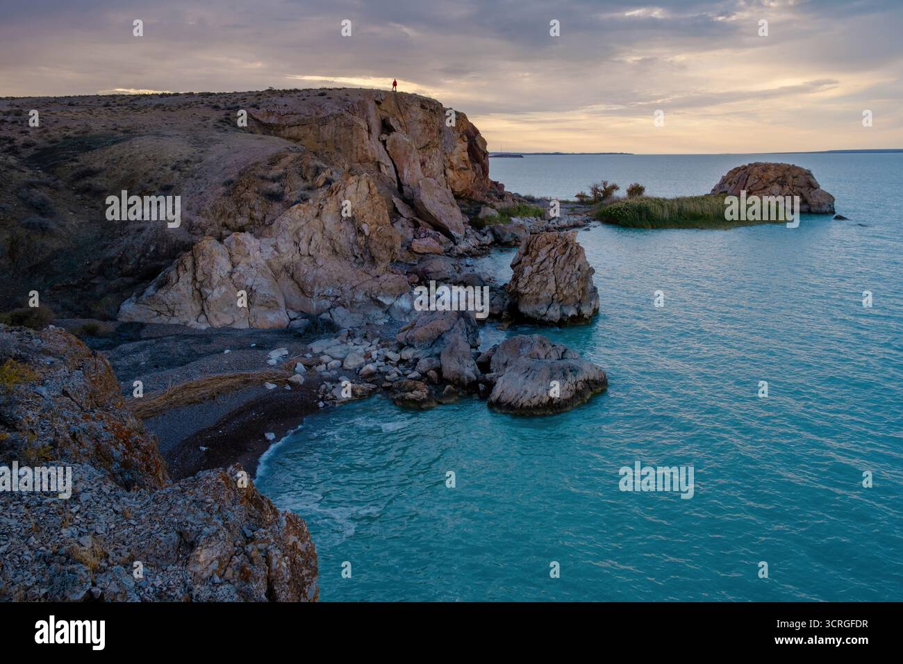Felsiges und wunderschönes Ufer des Balchash-Sees in Kasachstan mit türkisfarbenem Wasser an einem Herbsttag mit einem Mann auf den Felsen. Stockfoto