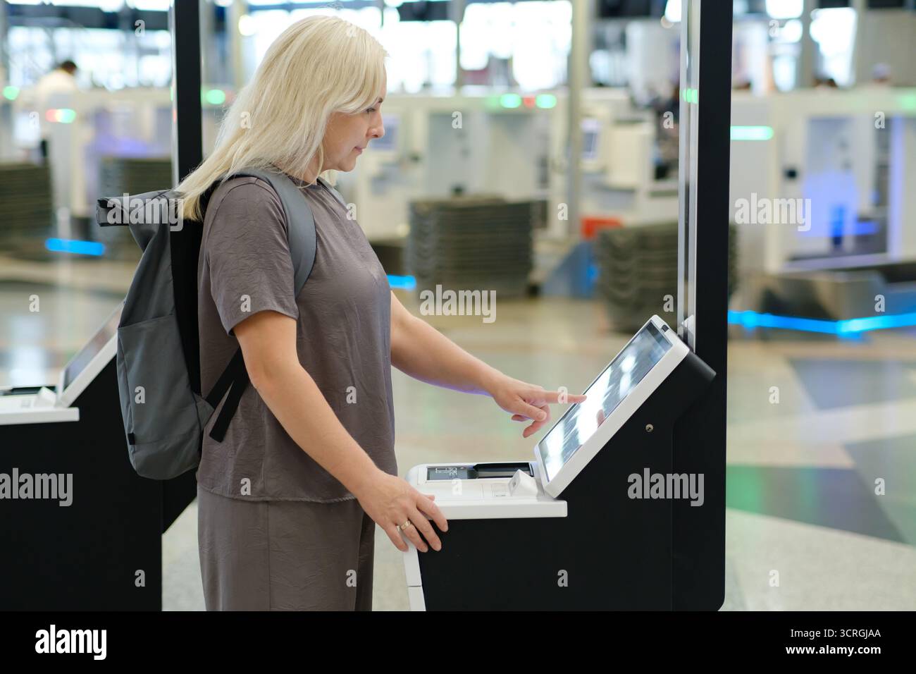Ein Reisender steht an einem Automaten zum Selbsteinchecken am Flughafen und bedient sich über den Touchscreen, um die Flugdaten zu verwalten, während er von anderen Passagieren und umgeben ist Stockfoto