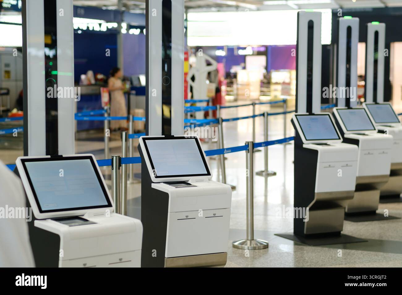 In einem eleganten, modernen Flughafenterminal befinden sich mehrere automatisierte Check-in-Automaten. Reisende werden beim Einchecken beobachtet, was die zunehmende Nutzung unterstreicht Stockfoto