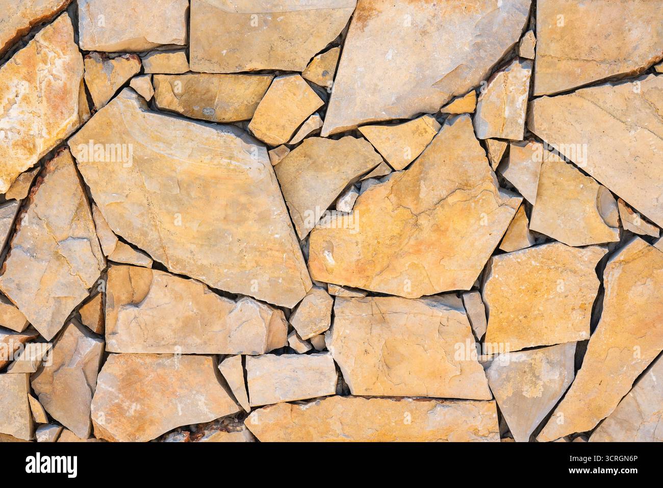 Unregelmäßige gelbe Steine bilden eine trocken verlegte Mauerwand mit natürlichen Rissen und Kanten. Stockfoto