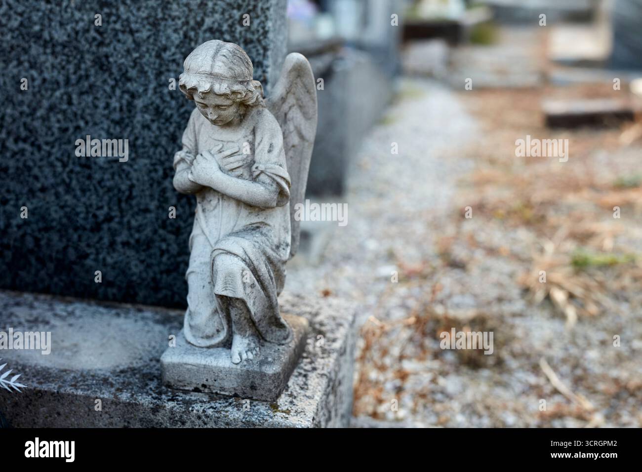 Eine kniende Engelsstatue ziert einen Grabstein auf einem Friedhof. Stockfoto