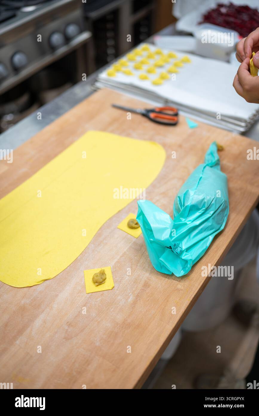 Frischer hausgemachter Nudelteig für Ravioli, gefüllt mit den Händen des Küchenchefs, die im Hintergrund zartere Nudelformen zubereiten Stockfoto