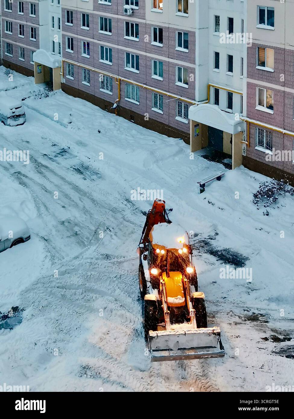 Der Traktor räumt Schnee auf einem Wohnhof im Winter, bei Straßenpflege und im Stadtverkehr Stockfoto
