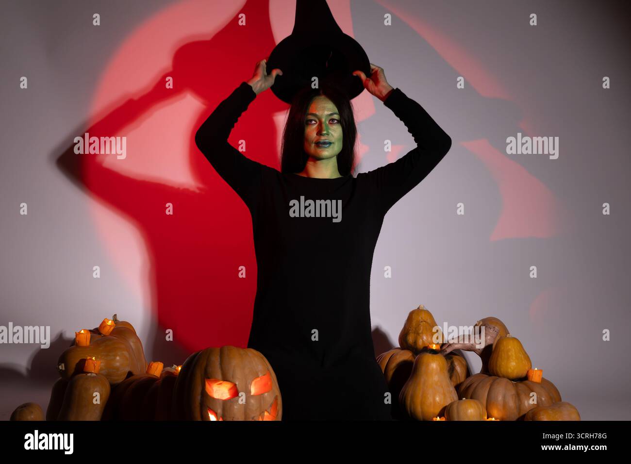 Frau in schwarzem Kleid und Hut, die elegant neben Kürbissen posiert, Herbstfarben Stockfoto